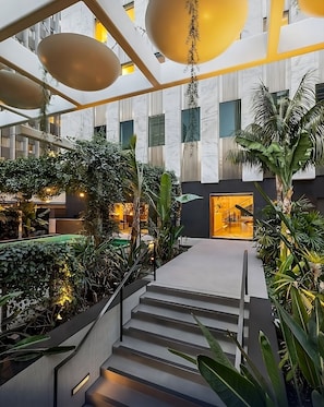 Un moderno atrio interior con una escalera central, rodeado de exuberante vegetación y un ambiente cálido y acogedor.
