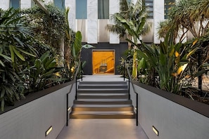 A modern staircase with a glass elevator entrance, surrounded by lush greenery. - Perfect LA Escape | Pool, Pets Allowed | Walt Disney Concert Hall - 0.9 mile (Los Angeles)
