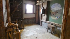 Ein rustikales Interieur mit Steinböden, einer Holztreppe, einem Fenster, einer Glocke und einem Gemälde von einer Kuh auf einem Berg.