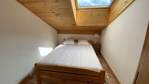 Ein kleines Schlafzimmer mit Holzrahmen, einem Oberlicht, einem Bett, einem Nachttisch und einer Lampe.