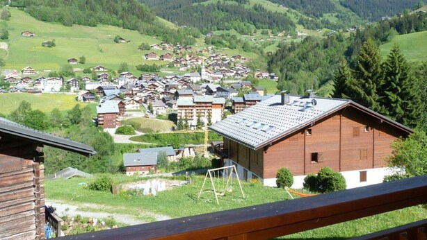 Ein Bergdorf mit traditionellen Holzhäusern, einer Seilbahn und Blick auf die umliegenden Hügel und Berge.