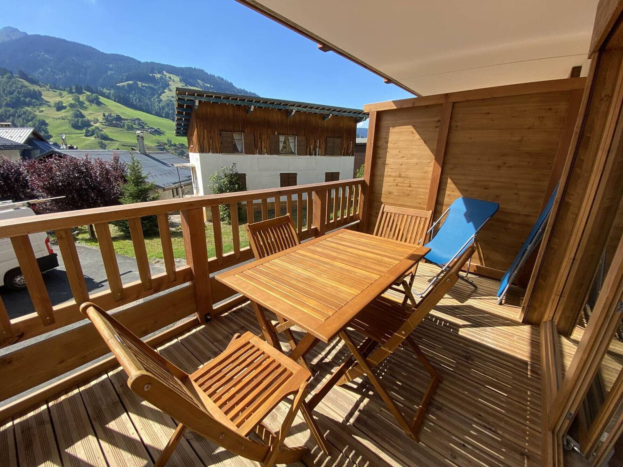 Una terraza de madera con una mesa y sillas, con vista a un paisaje montañoso.