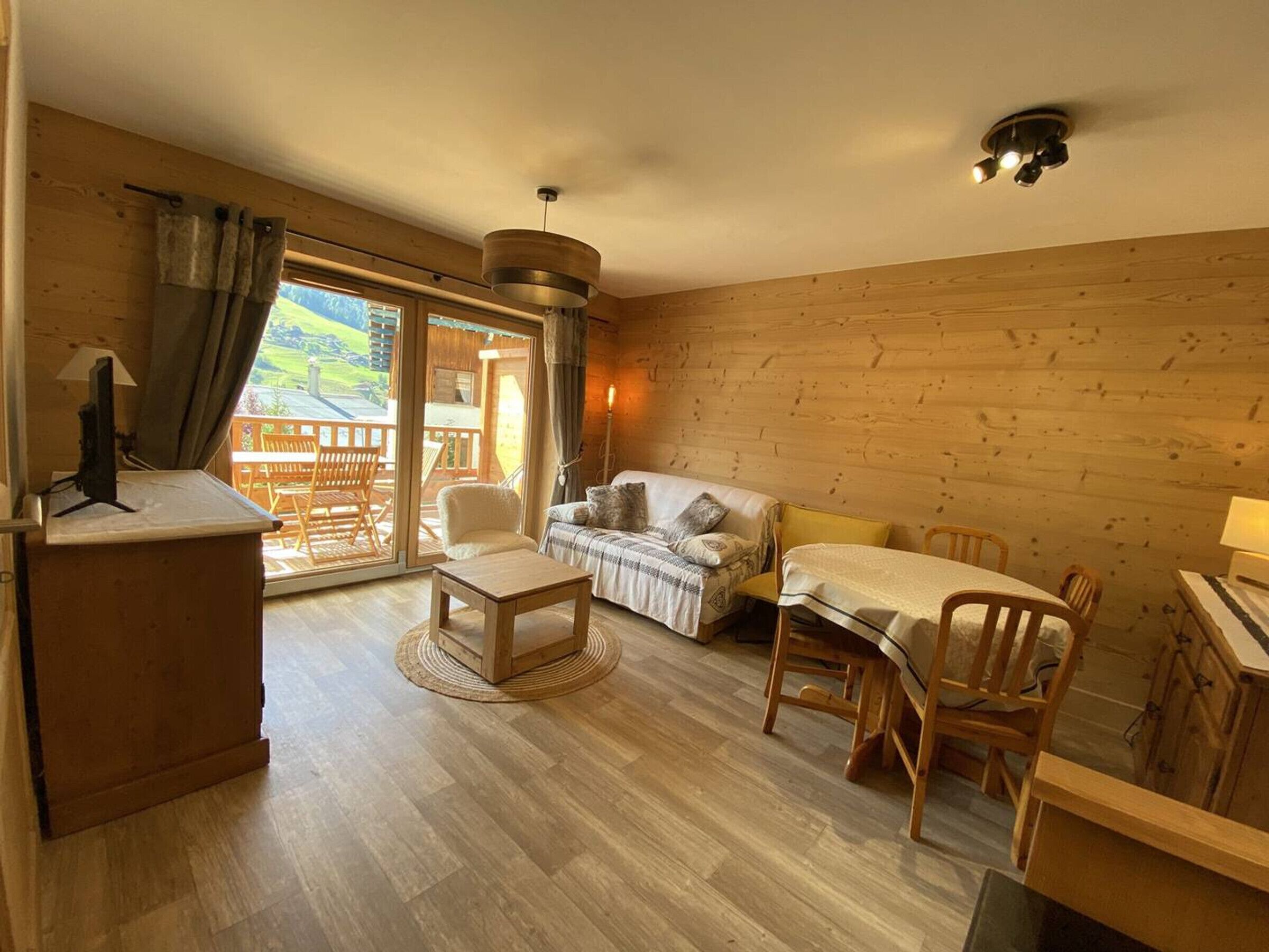 Ein gemütliches Zimmer mit einer Couch, einem Esstisch, Stühlen, einem Fernseher und einer Schiebetür zu einem Außenbereich.