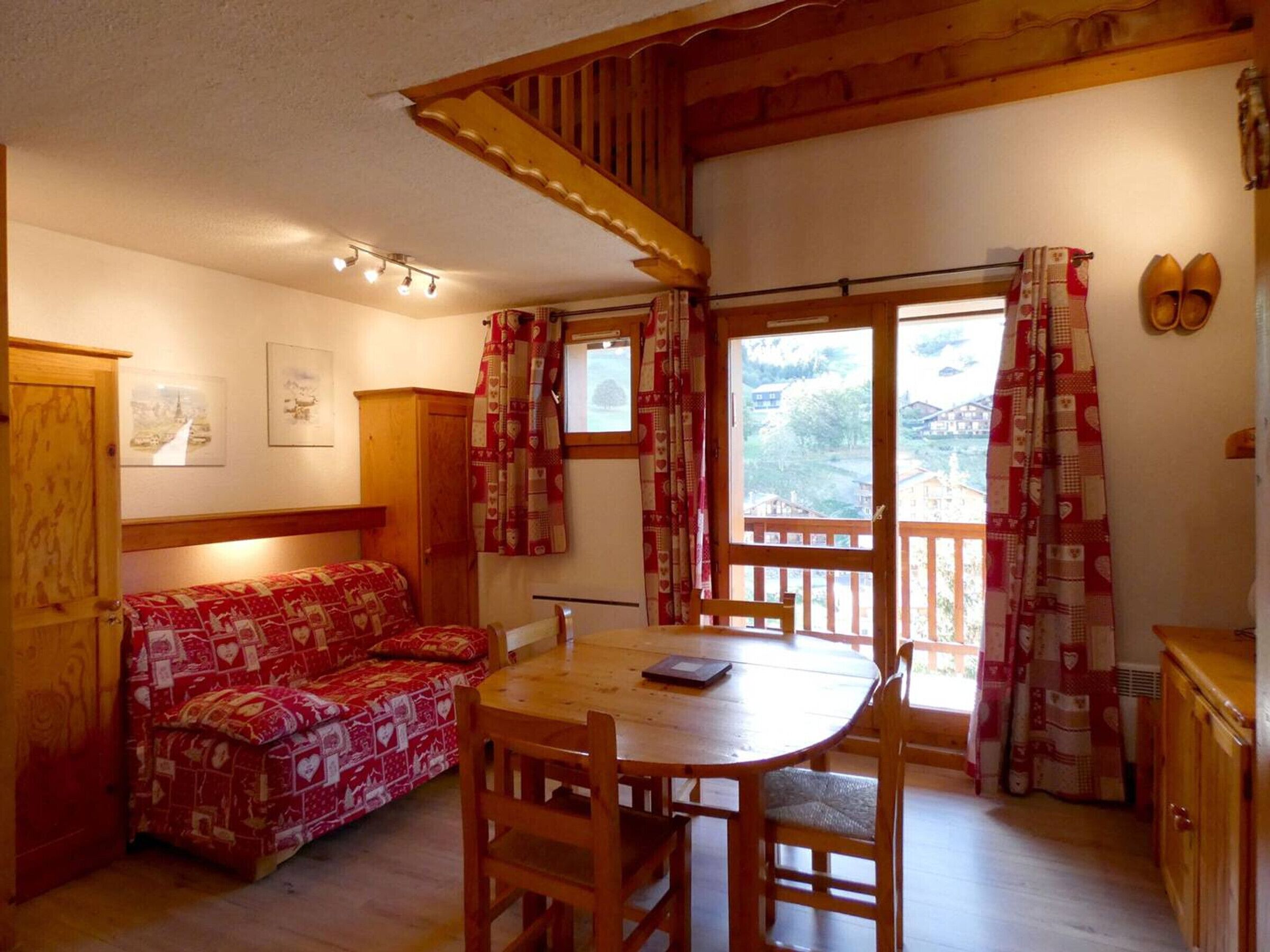 A cozy room with a wooden ceiling, a sofa, a dining table with chairs, and a window with curtains.