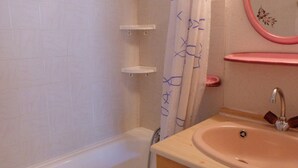Et badeværelse med badekar, vask med spejl og badeforhæng.