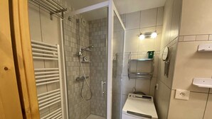 Een badkamer met een douche in een glazen cabine, een wit wastafelmeubel en een compacte wasmachine.