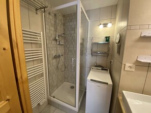 A bathroom with a glass-enclosed shower, a white sink, and a compact washing machine.