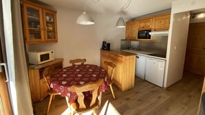 Een kleine keuken met houten kastjes, een magnetron, een spoelbak en een eettafel met stoelen.
