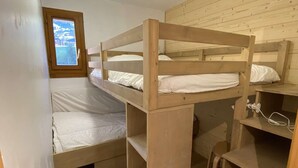 Een slaapkamer met stapelbed, raam, houten wanden en bureau met stoel.