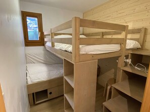 Ein Schlafraum mit Etagenbetten, einem Fenster, Holzwänden und einem Schreibtisch mit Stuhl.