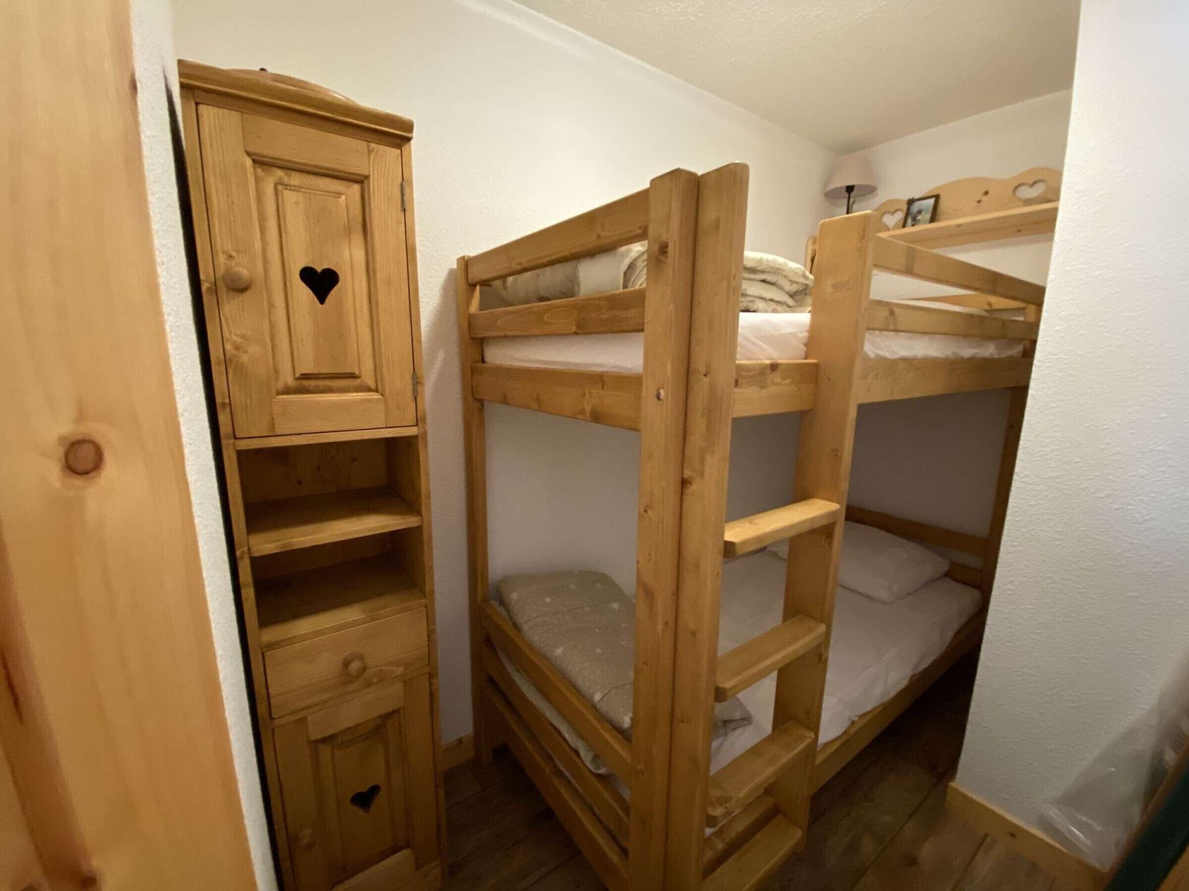 Un letto a castello con un'armadietto in legno e una piccola cassettiera con una ghirigora a forma di cuore.