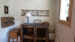 Een rustieke kamer met een houten bureau, een klein krukje en een plank met ingelijste foto's.