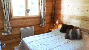 Een houten kamer met een bed, een kachel, gordijnen en een raam.
