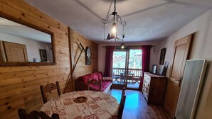 Un interior de madera con una mesa de comedor, sillas, un sofá, un balcón con vistas y un refrigerador.