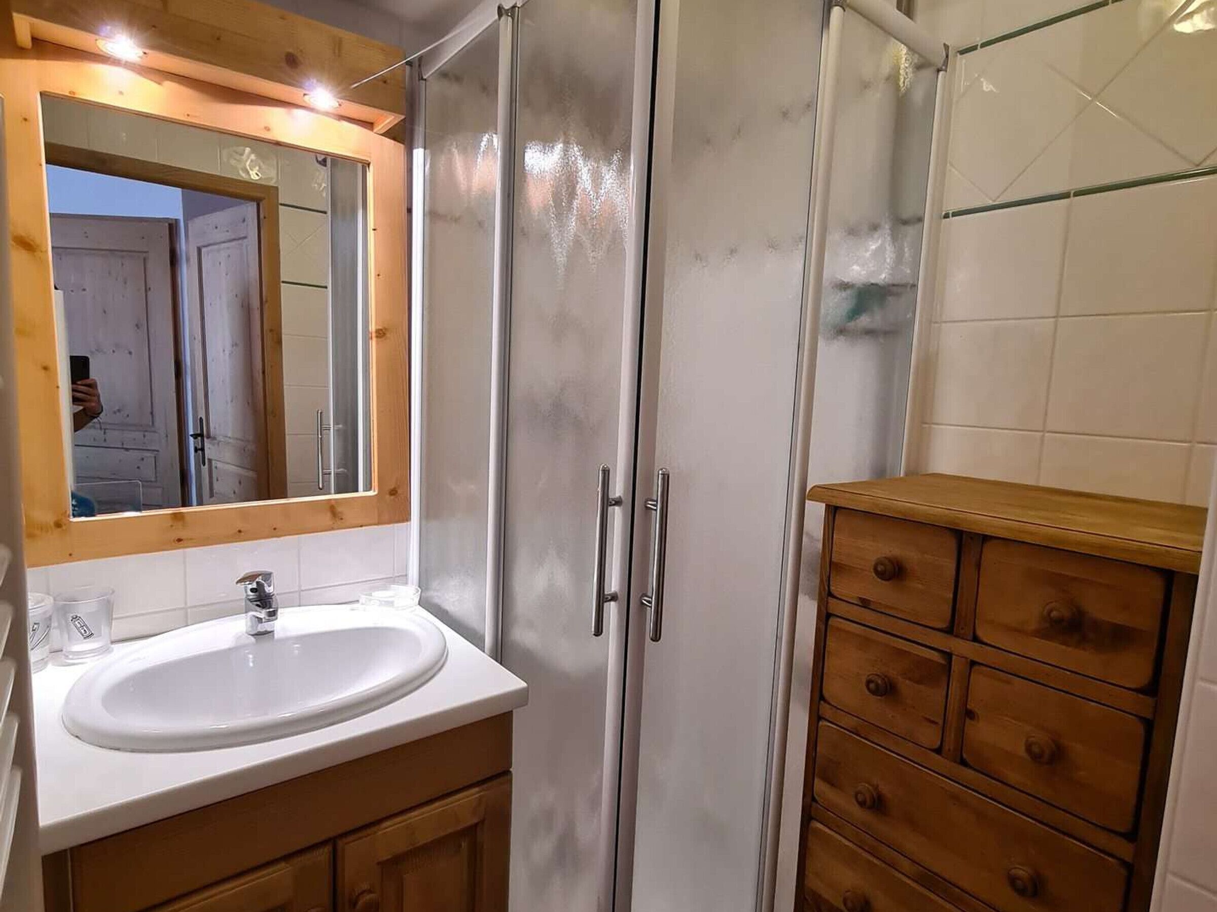 A bathroom with a white sink, wooden vanity, and a mirror with a wooden frame.