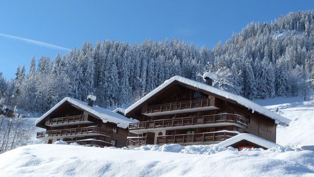 Una cabaña de madera con varios balcones, rodeada de árboles cubiertos de nieve.