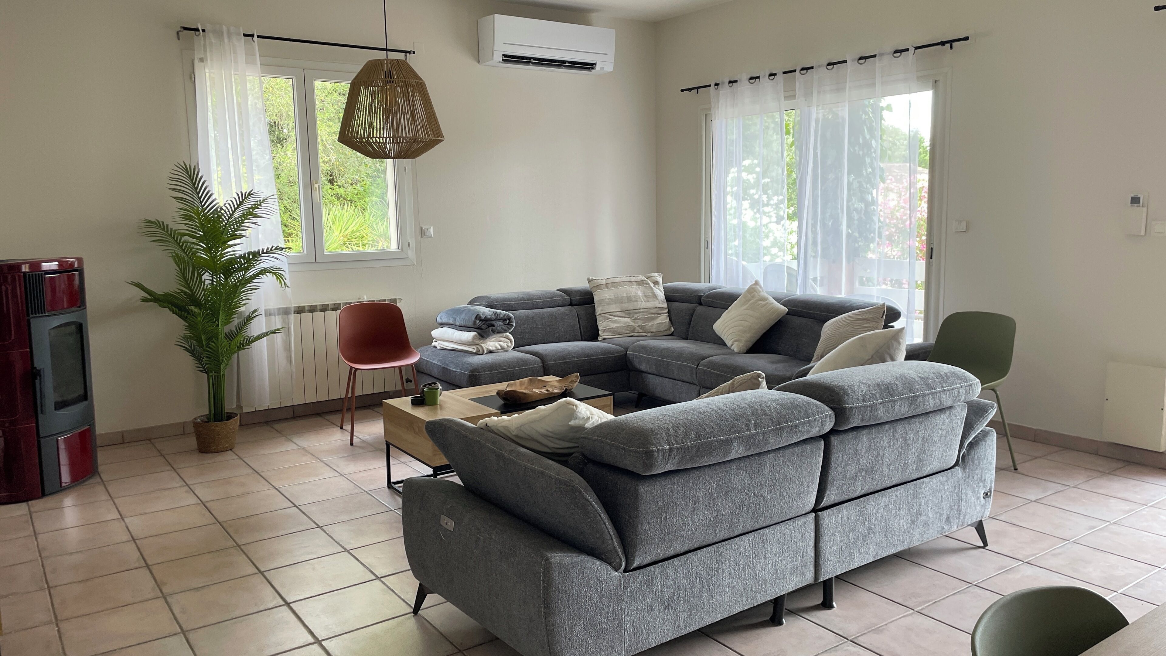 A modern living room with a grey sectional sofa, a wooden coffee table, a potted plant, and a hanging light fixture.