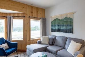 A modern living room with a sectional sofa, a blue armchair, and a round coffee table. - Suite 5 at The Gem | Bright 2BR Stay for Groups (Harvie Heights)