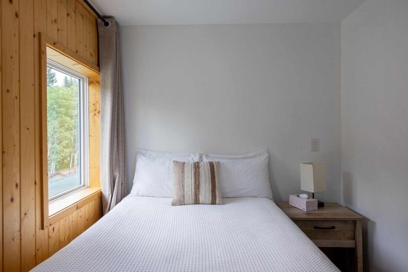 Una camera da letto con un letto, un comodino, una lampada e una finestra con tende.