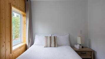 Een slaapkamer met een bed, nachtkastje, lamp en raam met gordijnen.