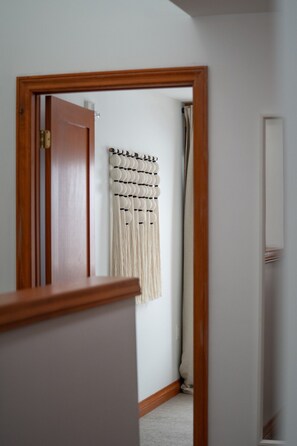 A hallway with a wooden door, a macrame wall hanging, and a mirror on the wall.