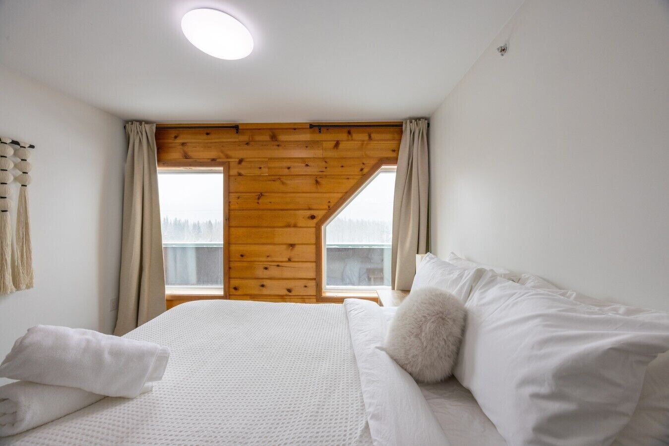 Een slaapkamer met een bed, kussens, een raam met gordijnen en een houten plafond.