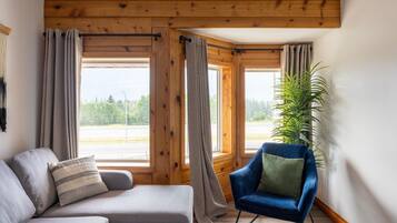 A cozy room with a sofa, a blue armchair, and a large window with curtains.