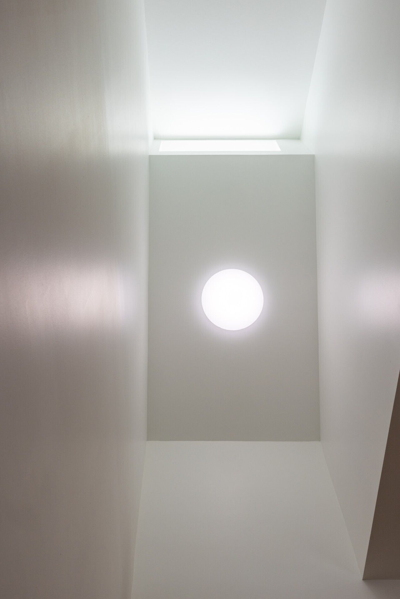 Una stanza con una luce a incasso nel soffitto e una parete bianca.