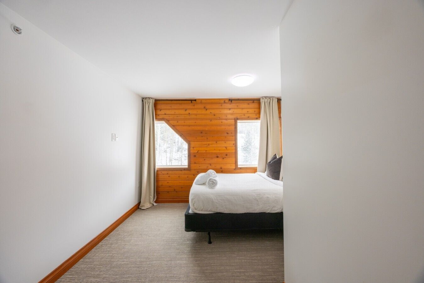 Um quarto com uma cama, janela, paredes de madeira e piso coberto por carpete.