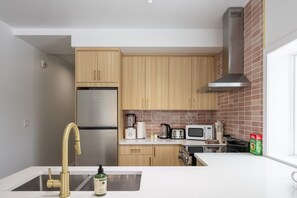 Eine moderne Küche mit Holzschränken, einem Edelstahlkühlschrank, einer Mikrowelle und einer Kaffeemaschine.