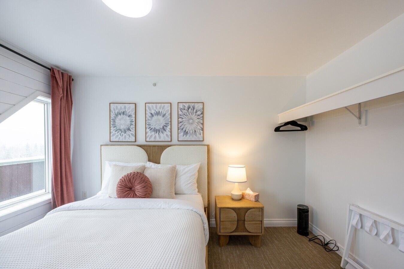 Ein Schlafzimmer mit einem Bett, einem Nachttisch mit Lampe und drei an der Wand hängenden Bildern.
