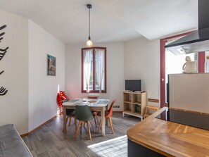 Una cuina moderna amb zona de menjador, terres de fusta, televisió i finestra amb cortines.