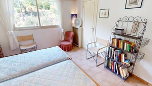 Een kamer met twee bedden, een stoel, een boekenplank en een raam met gordijnen.