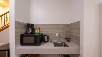 Una cocina compacta con microondas integrado, cafetera y pileta.
