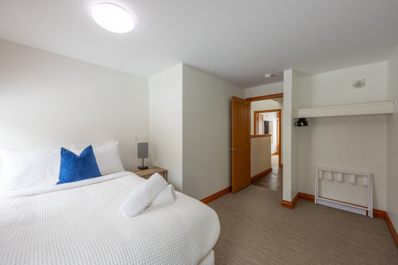 A hotel room with a bed, a bedside table, a lamp, a door leading to a hallway, and a radiator.