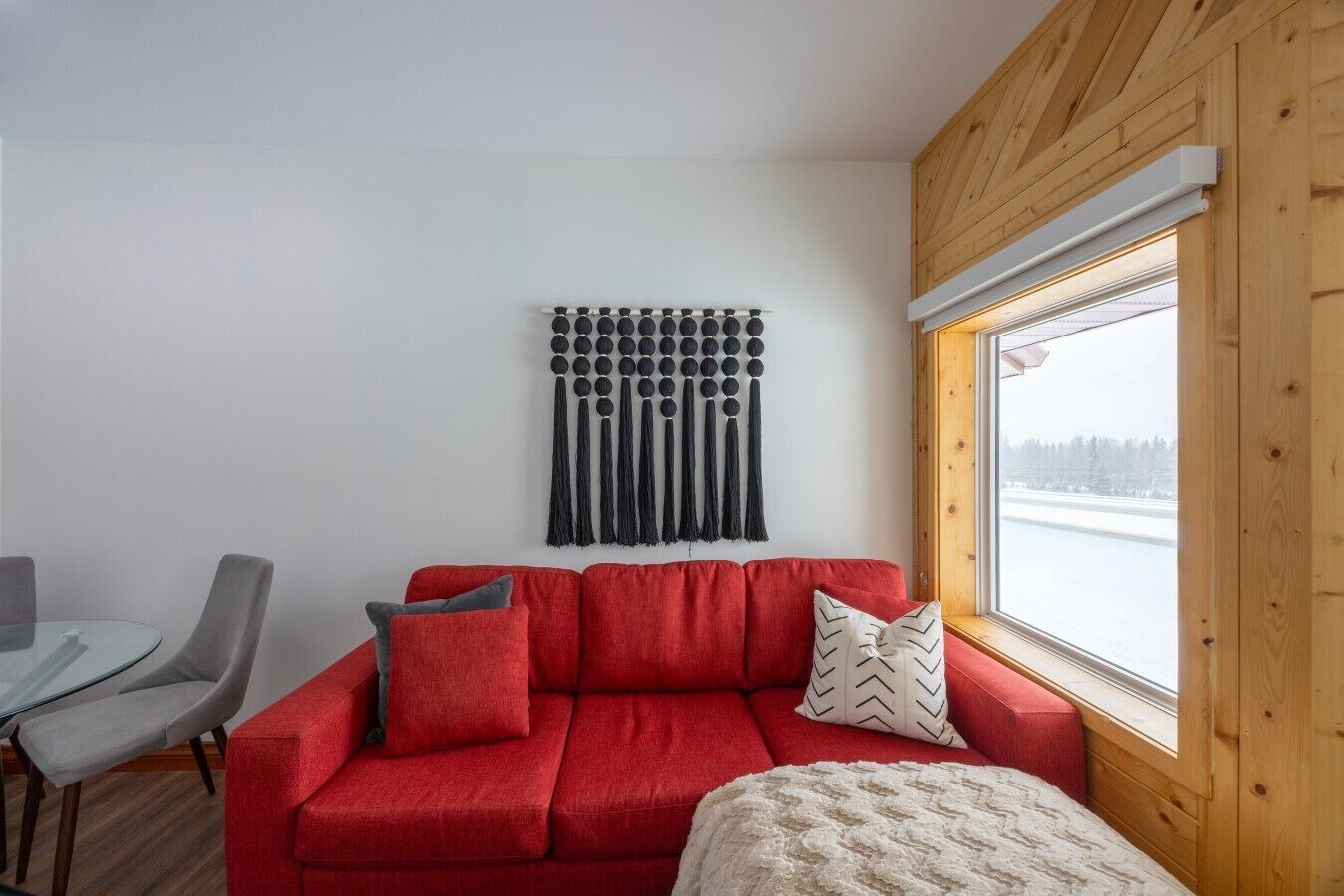 Un sofá rojo con cojines, una mesa de vidrio y sillas en una habitación con techo de madera y ventana con vista a un cuerpo de agua.