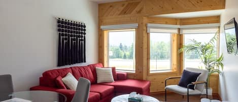 A modern living room with a red sofa, a grey armchair, a round coffee table, and a wooden ceiling.