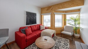 Un salon moderne avec un canapé rouge, une petite table ronde et un fauteuil blanc. Une grande fenêtre offre une vue sur un paysage enneigé.
