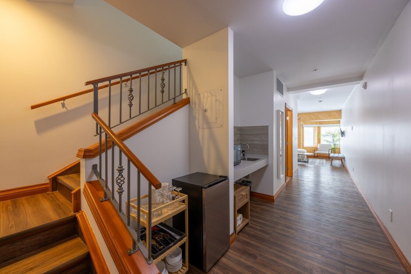 A modern interior with a wooden staircase, a kitchen area, and a hallway leading to a living space.
