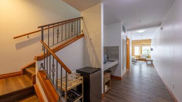 A modern interior with a wooden staircase, a kitchen area, and a hallway leading to a living space.
