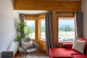 Une pièce avec un canapé rouge, un fauteuil gris et une grande fenêtre avec des rideaux.