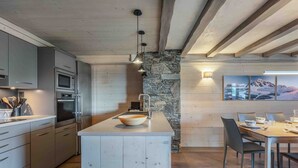 A modern kitchen with a central island, built-in appliances, and a dining area with a stone accent wall and artwork. - Family apartment, balcony - 6 guests (Méribel)