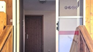 Eine Holztreppe führt zu einem Raum mit einer Tür und einer Glaswand, an der keine Fenster erkennbar sind.