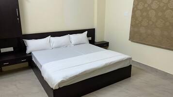 Uma cama de solteiro com cabeceira escura, mesa de cabeceira, guarda-roupa e cortina estampada.