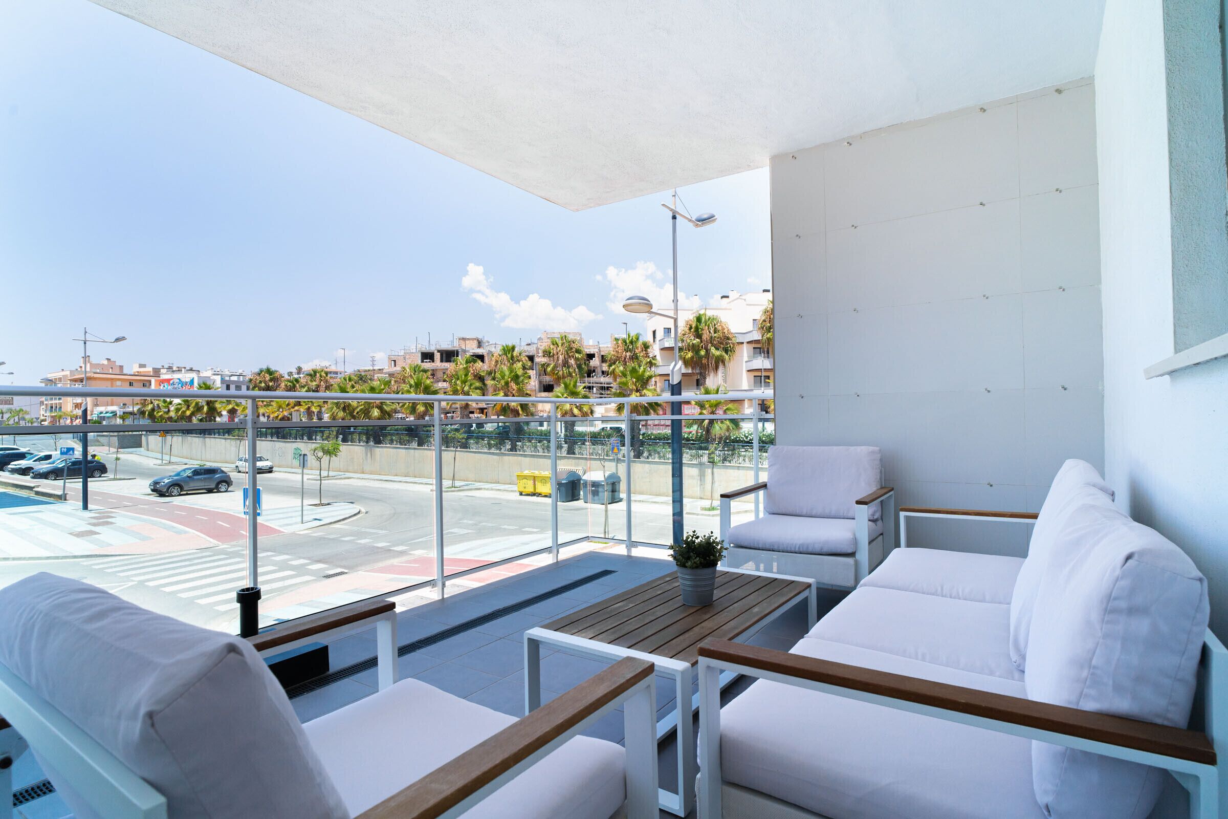A balcony with white furniture, a view of the street, and a clear sky.