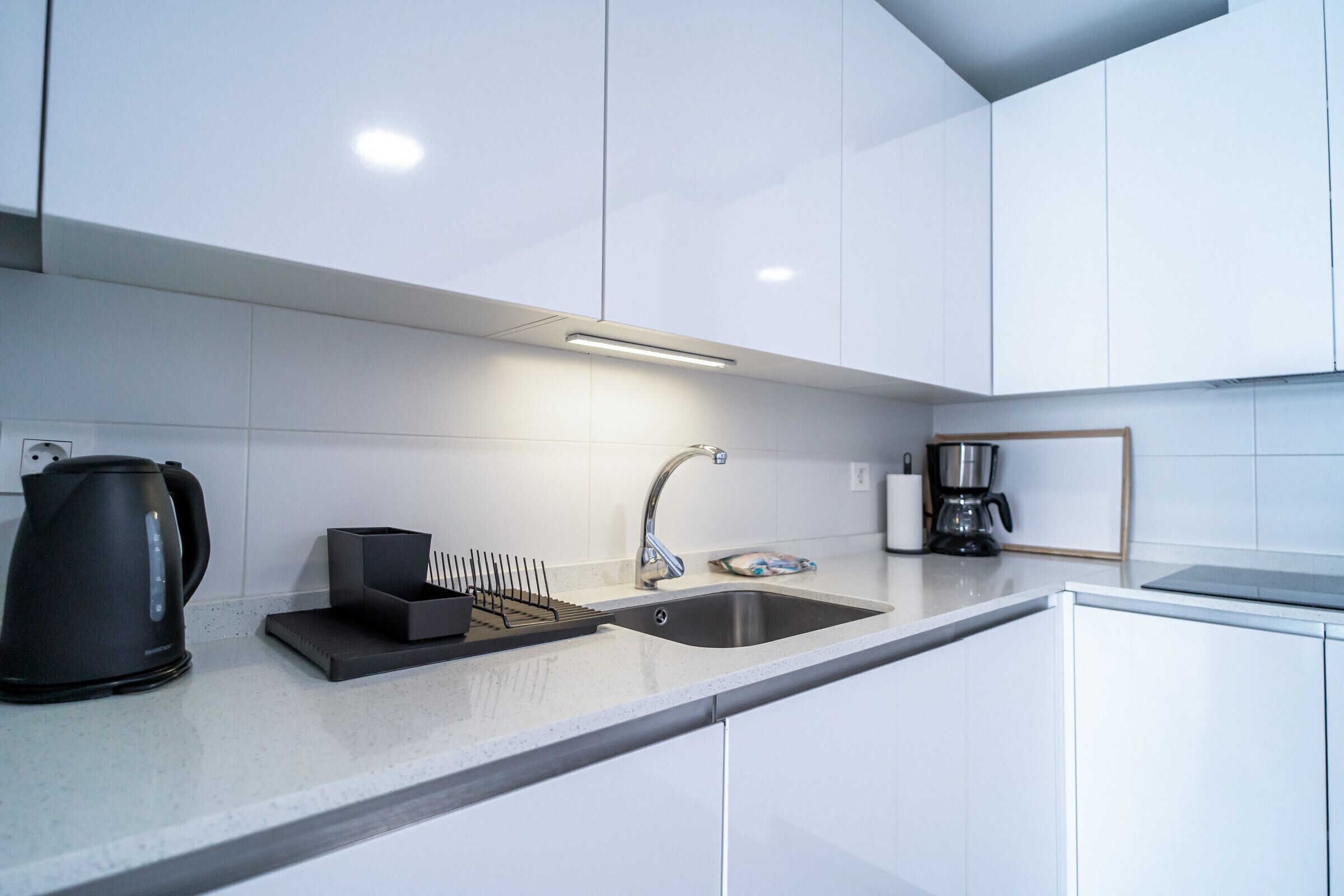 A modern kitchen with white cabinets, a stainless steel sink, a coffee maker, and a kettle.