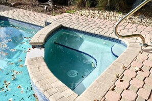 Ein Pool mit gefliestem Rand, einer integrierten Whirlwanne und einer Metallhandläufe.