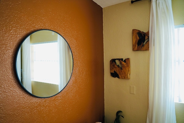 Una stanza con uno specchio rotondo, opere d'arte al muro e una finestra con tende.