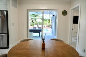 A dining area with a wooden table, a vase with a plant, and a view of an outdoor patio with chairs and a table. - Luxury Escape w/ Pool & Billiards • Near Beach (Hollywood)