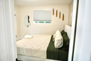 Ein Schlafzimmer mit einem Bett, einem Fenster, einem Spiegel und Wandpflanzen.